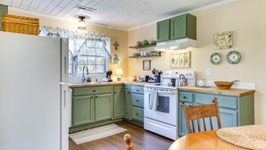 A kitchen with green cabinets, a white refrigerator, a stove, and a dining table with chairs.