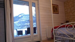 Une chambre à coucher avec un lit, une fenêtre donnant sur les montagnes, un mur en pierre et une porte.