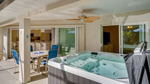 Un bain à remous doté d’un ventilateur de plafond, un coin repas avec des chaises et une table, et une cuisine visible à travers des portes vitrées.