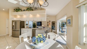 Une cuisine spacieuse avec des meubles blancs, un réfrigérateur en acier inoxydable et un coin repas avec une table dressée pour deux personnes.