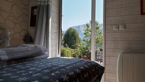 Une chambre à coucher avec un lit, une table de chevet, une lampe et une vue sur les montagnes, visible à travers une porte-fenêtre coulissante.