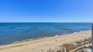 Une vue sur la plage, avec un ciel dégagé, une plage de sable et un bâtiment au premier plan.