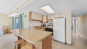 A modern kitchen with a central island, wooden cabinets, a refrigerator, and a microwave. - Summer Beach 801 by Seaside Vacations & Sales (Ocean City)