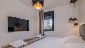 Una habitación de hotel moderna con una cama grande, un televisor de pantalla plana y un ventanal con cortinas.