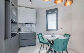 A modern kitchen with grey cabinets, a white countertop, and a round table with teal chairs.
