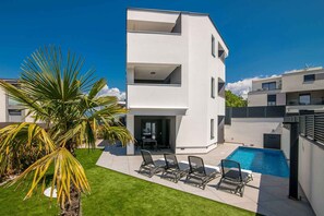 A modern multi-story building with a swimming pool, outdoor seating, and a palm tree.