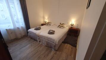 Un letto matrimoniale con piumone bianco, due cuscini e un comodino con una lampada.