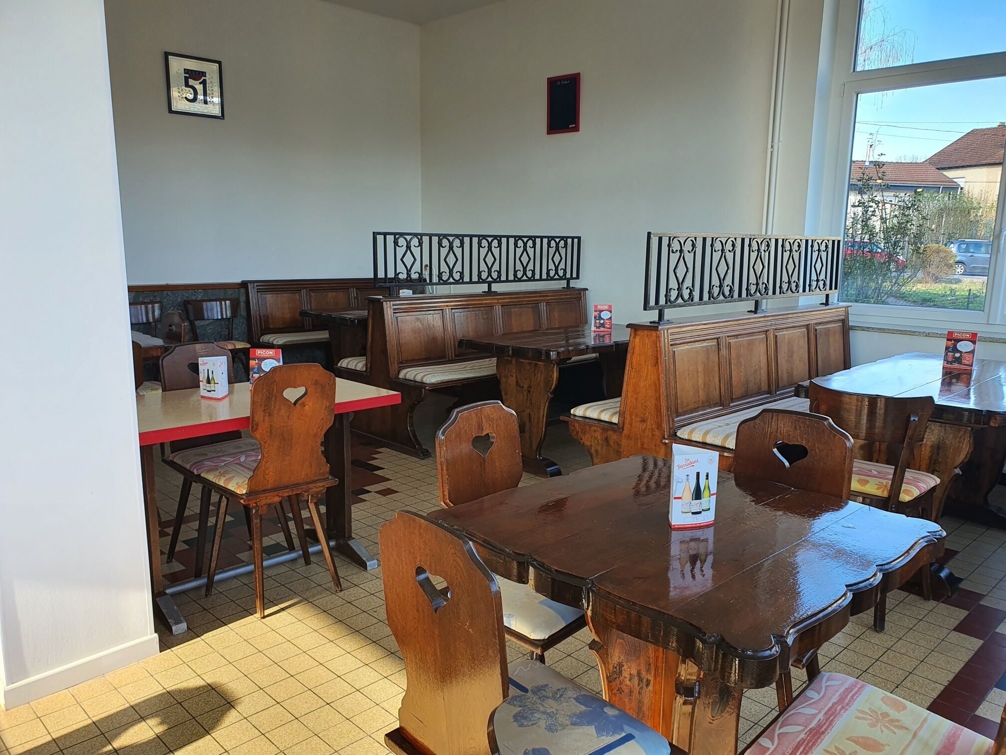 A restaurant with wooden tables and chairs, a tiled floor, and a view through a window.