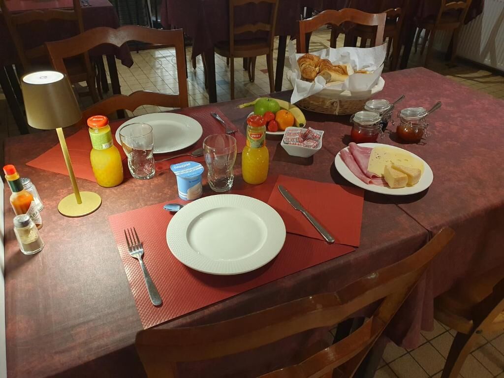 Ein Esstisch, gedeckt mit Tellern, Besteck, einer Orangensaftflasche, einem Glas Wasser, einem Korb mit Croissants und einer Platte Käse und Schinken.