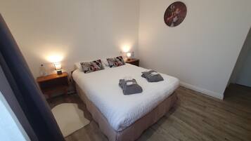 Ein ordentlich eingerichtetes Schlafzimmer mit einem großen Bett, zwei Nachttischen mit Lampen, einer Wanduhr und einem Holzboden.