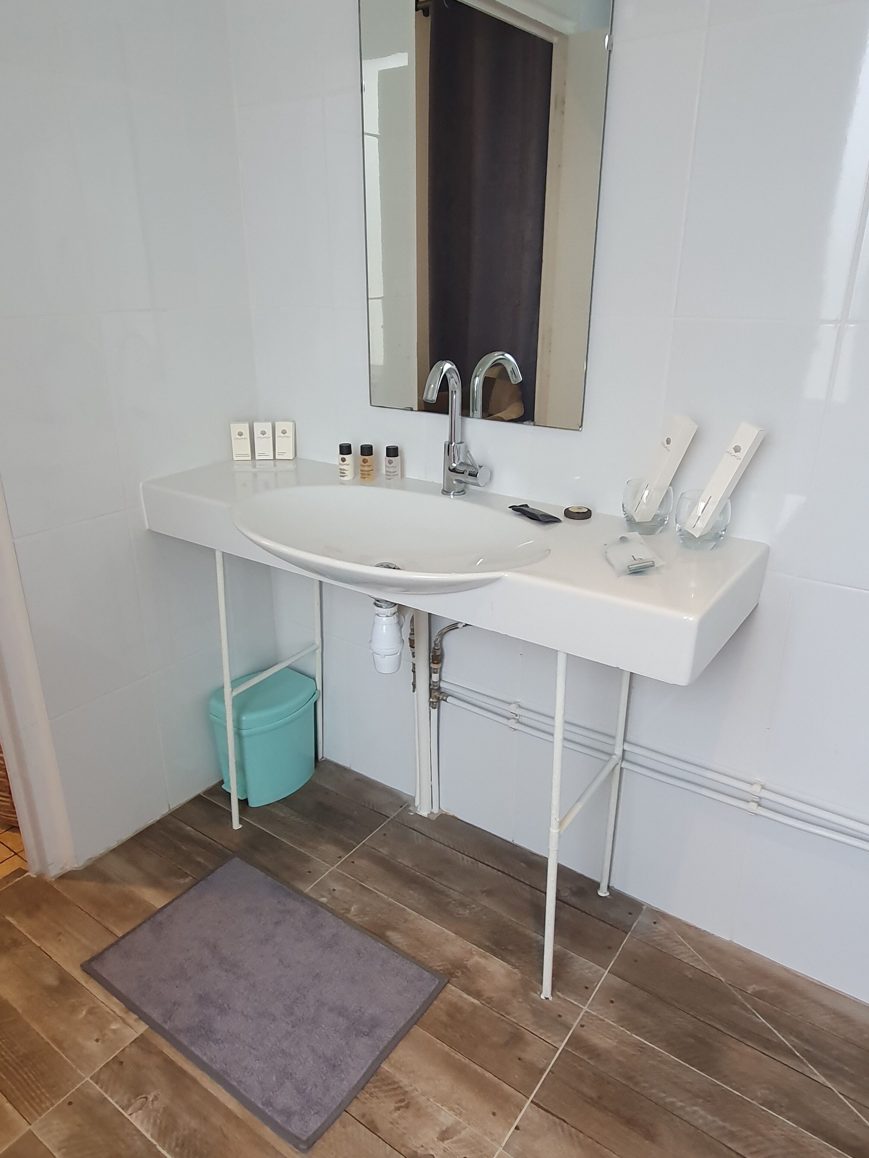 Une salle de bain avec un lavabo blanc, un miroir et une petite poubelle.