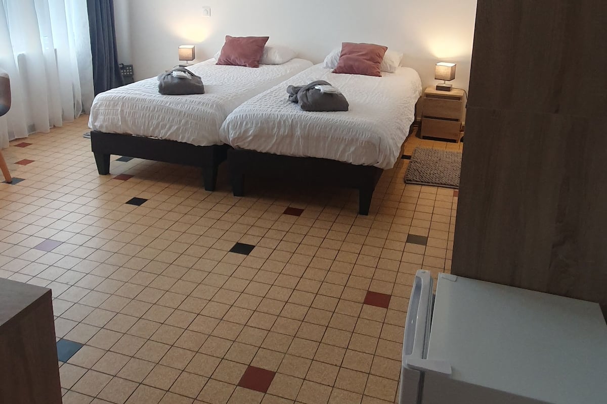 A hotel room with two beds, a small table, and a nightstand with a lamp.