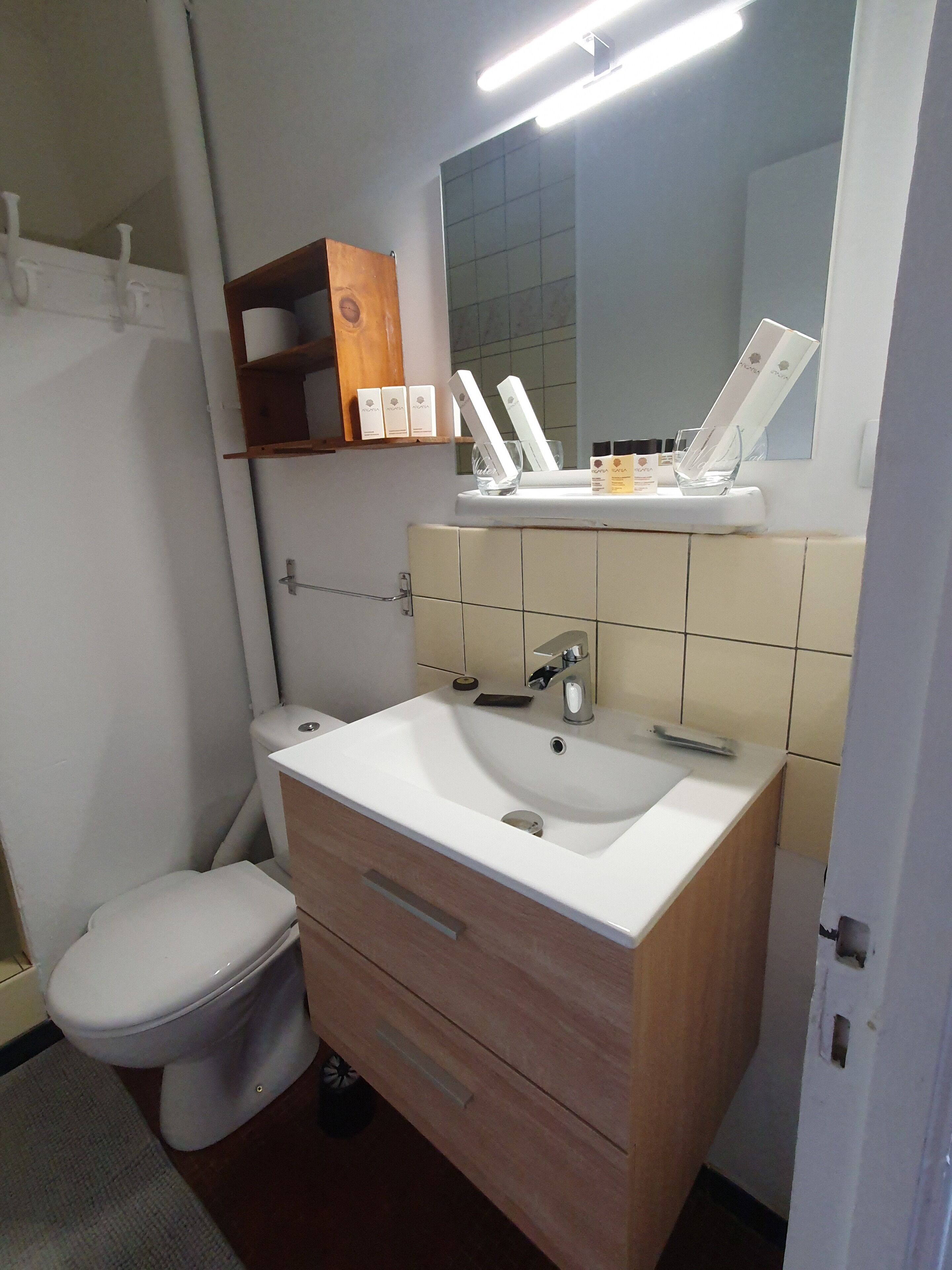 Een badkamer met een witte wastafel, houten wastafelmeubel en een spiegel erboven.