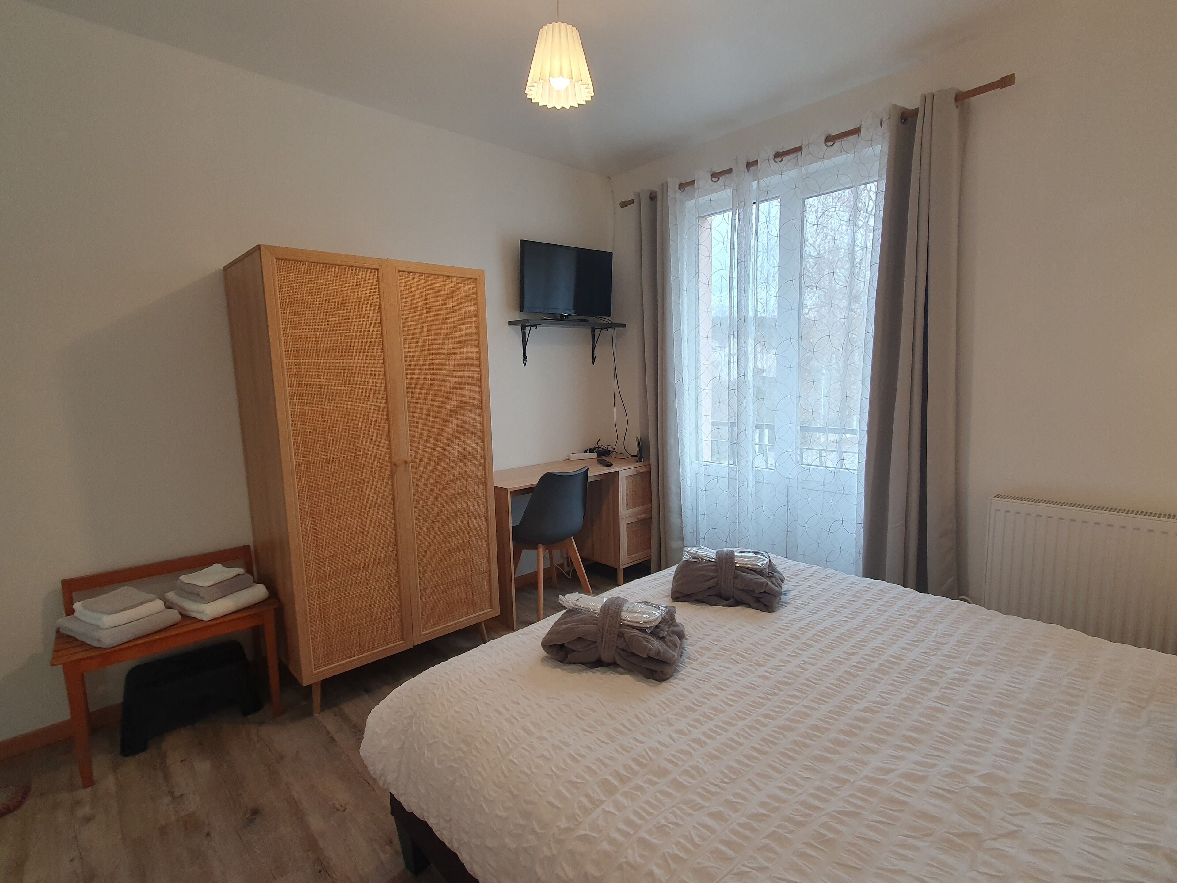A hotel room with a bed, a desk with a chair, a wardrobe, and a television on the wall.