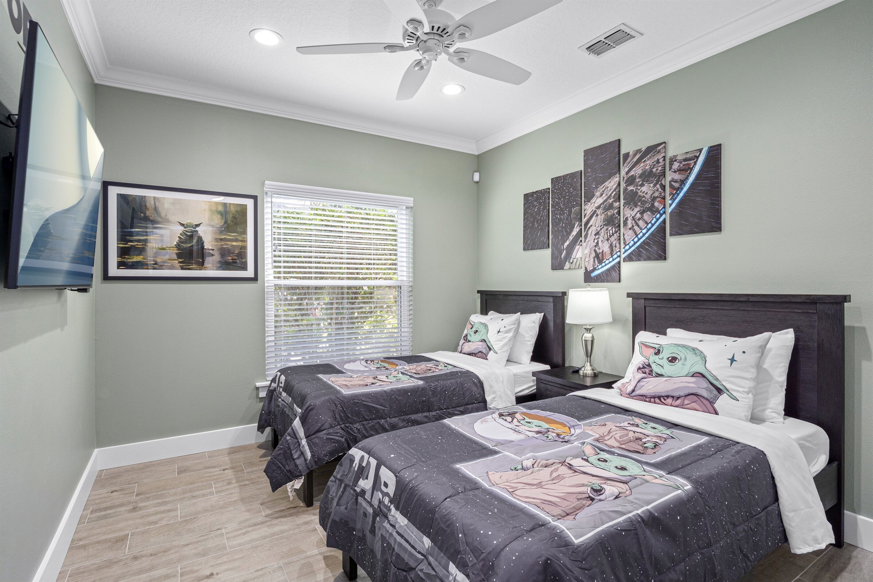 A bedroom with two beds, a ceiling fan, a window with blinds, and wall art.