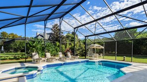 A covered swimming pool with lounge chairs and a hot tub, surrounded by a metal frame and glass panels.