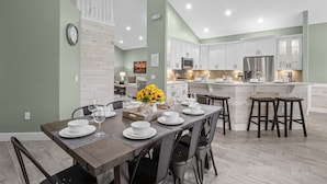 A modern kitchen with white cabinets, a stainless steel refrigerator, and a dining area with a wooden table set for four.