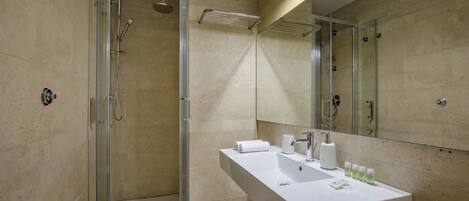 Un baño moderno con ducha de vidrio, un lavabo blanco con artículos de aseo y un espejo grande.