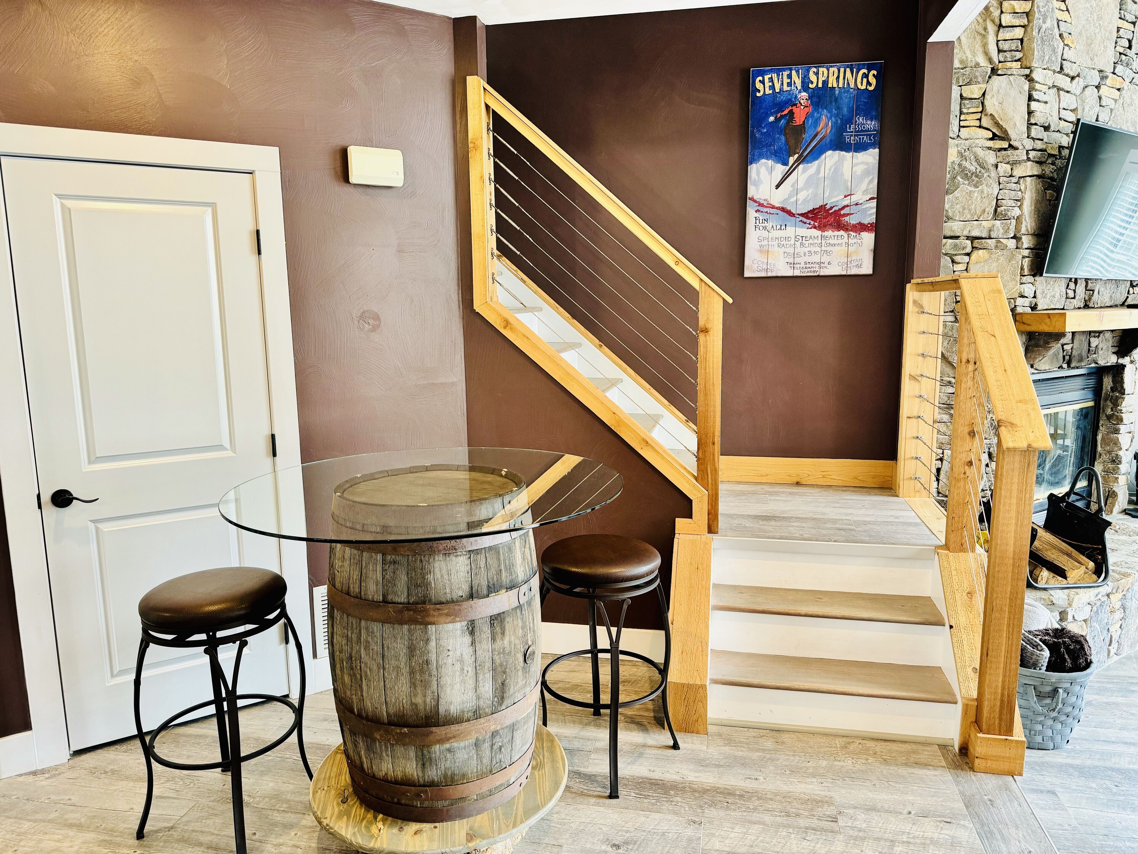 A staircase with wooden railings, a poster on the wall, and a rustic barrel as a table centerpiece.