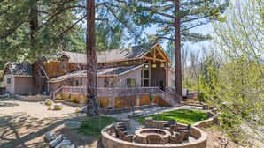 A lodge with a large deck, stone fire pit, and a well-maintained lawn.