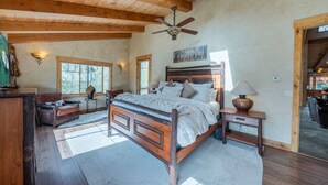 A bedroom with a wooden ceiling, a bed with a headboard, a nightstand, a lamp, and a chair.