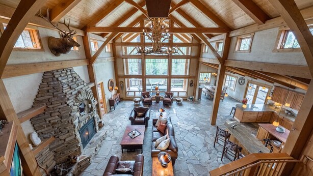 A spacious lodge with a stone fireplace, leather seating, and a large wooden ceiling.