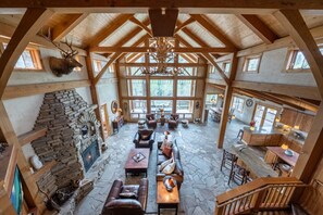 A spacious lodge with a stone fireplace, leather seating, and a large wooden ceiling.