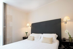 Una habitación de hotel con una cama grande, dos mesitas de noche, una lámpara y un florero con flores.