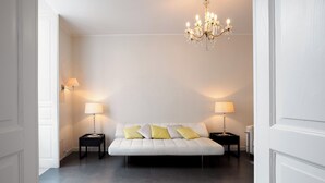A modern bedroom with a white bed, two bedside tables with lamps, and a chandelier. - Hotel Palazzo Cavalieri (Syracuse)