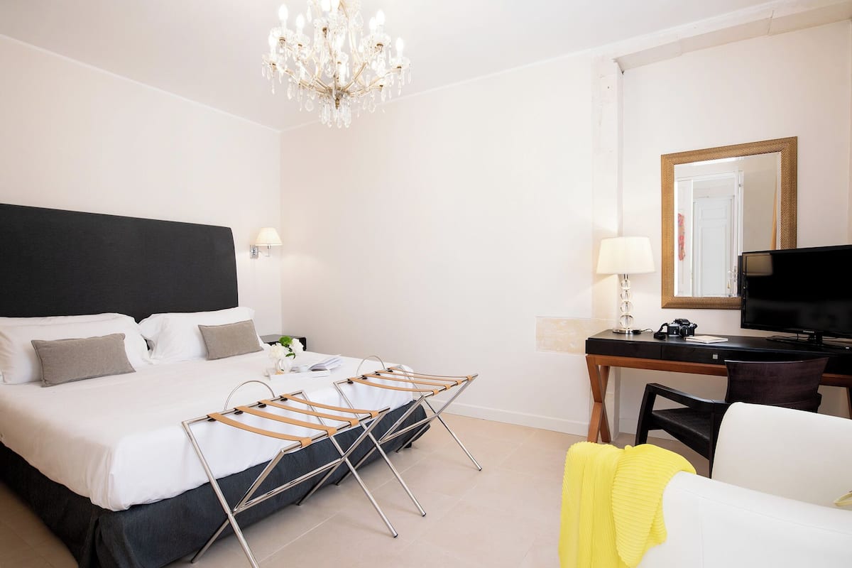 Une chambre d’hôtel avec un lit, un bureau, une chaise, un miroir et un lustre.