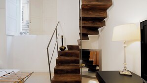 A modern staircase with a wooden finish, a black vase on the landing, and a lamp on the right. - Hotel Palazzo Cavalieri (Syracuse)