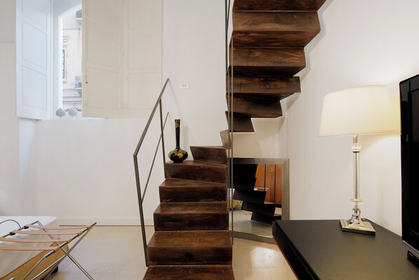 A modern staircase with a wooden finish, a black vase on the landing, and a lamp on the right.