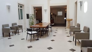 A dining area with a wooden table and chairs, a potted plant, and a tiled floor with a geometric pattern. - Hotel Palazzo Cavalieri (Syracuse)