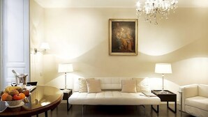 A modern living room with a sofa, two side tables, a chandelier, and a painting on the wall. - Hotel Palazzo Cavalieri (Syracuse)