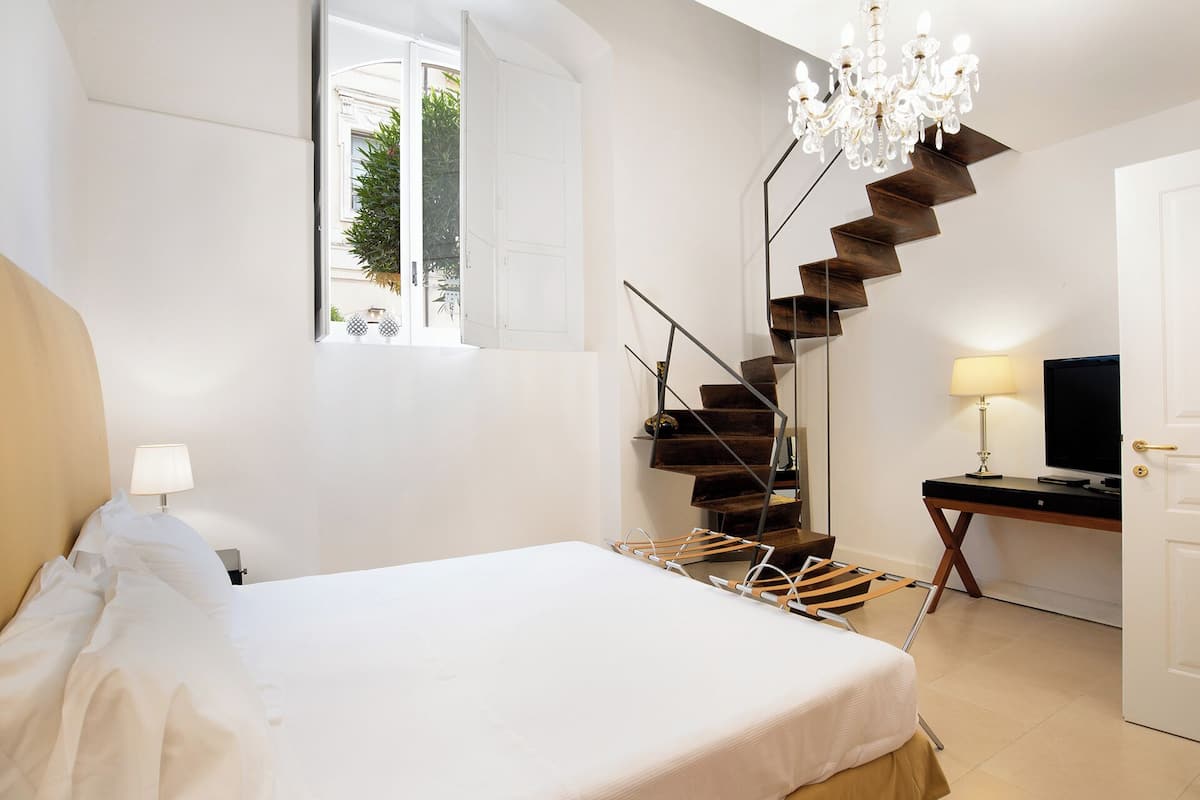 Une chambre à coucher avec un lit, un bureau avec une télévision, un lustre et un escalier en colimaçon.