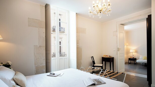 A hotel room with a large bed, a chair, a small table, and a chandelier. - Hotel Palazzo Cavalieri (Syracuse)