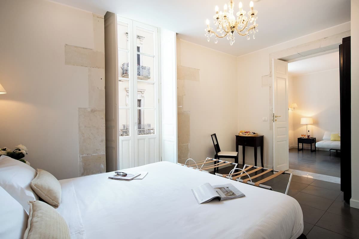 Une chambre d’hôtel avec un grand lit, une chaise, une petite table et un lustre.