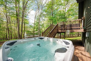 Ein Whirlpool inmitten von Bäumen mit einer Holzterrasse und Treppe, die zu einem Haus führt.