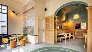 A spacious hotel lobby with a mural, wooden furniture, and a green carpet. - Made in Catherine (Brussels)