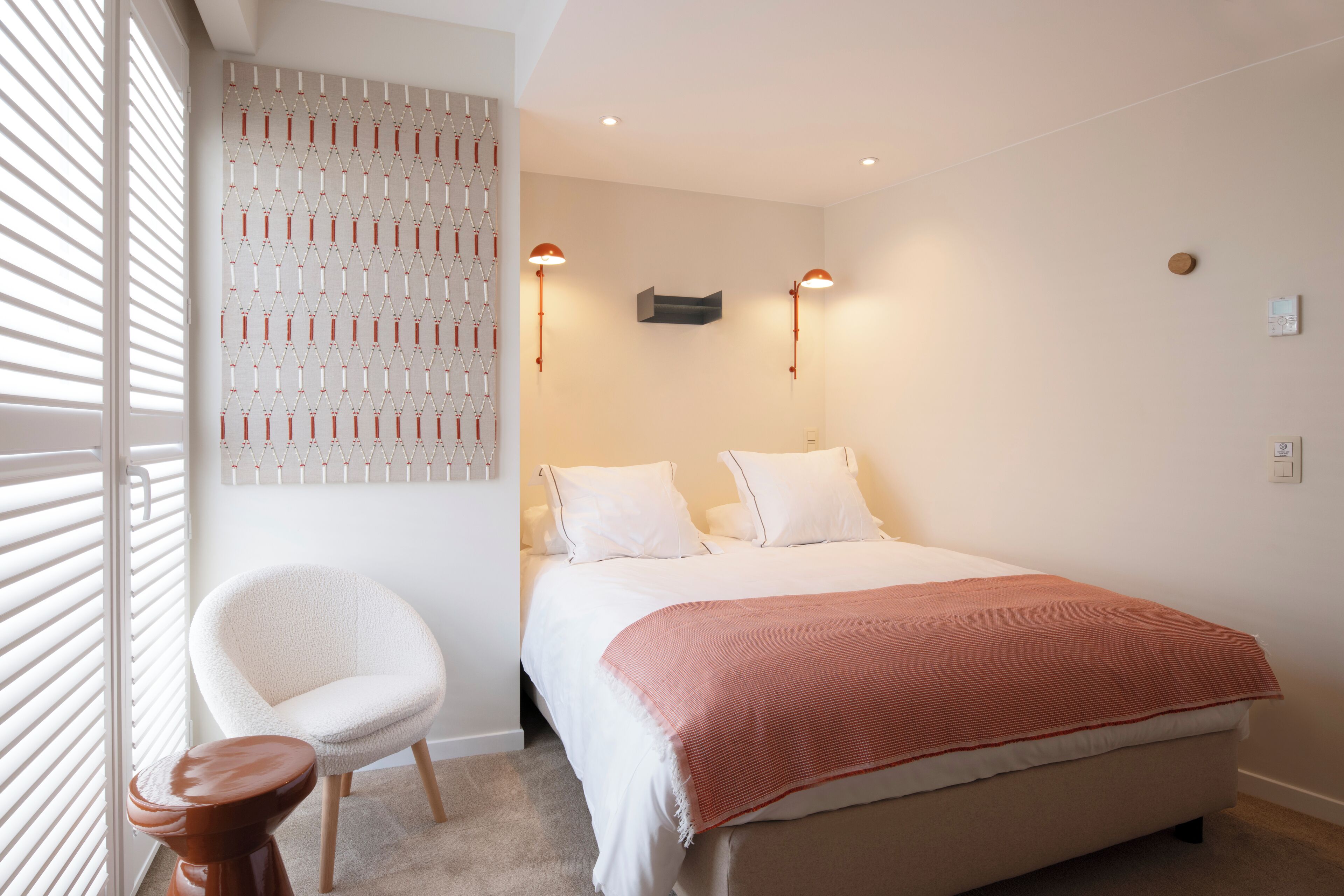 A bedroom with a bed, a chair, and a wall-mounted light fixture.