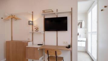 A modern, compact room with a wooden desk, a chair, a TV, and a small shelf with a basket.