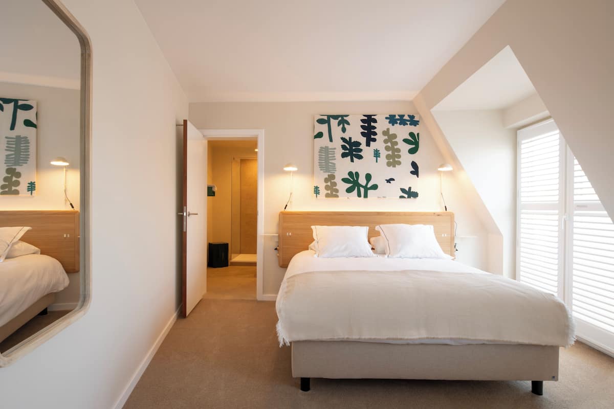 A bedroom with a large bed, a mirror, and a wall with abstract art.