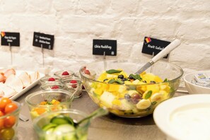 Un bufé con diversas opciones de comida, incluyendo un bol de ensalada de frutas, yogur y un plato de almendras laminadas.