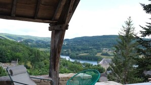 Une terrasse offrant une vue sur un lac et des collines, avec deux chaises et un mur en pierre.