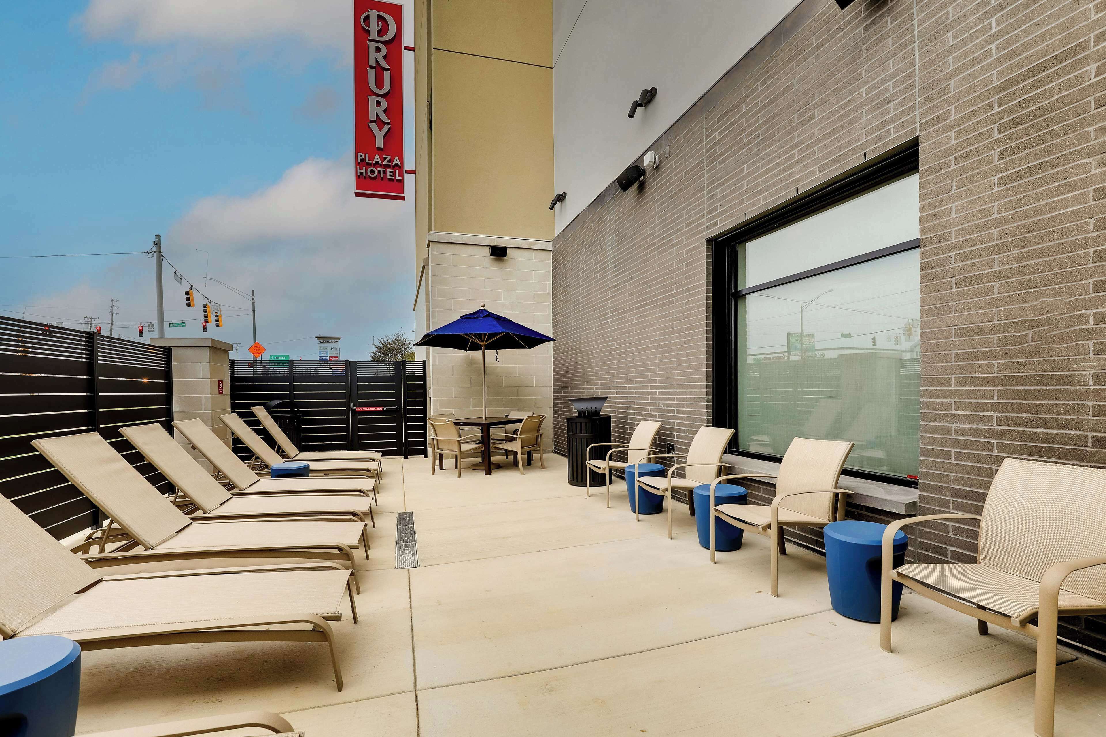 A Drury Plaza Hotel outdoor seating area with lounge chairs, a table, and an umbrella.