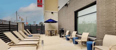A Drury Plaza Hotel outdoor seating area with lounge chairs, a table, and an umbrella.