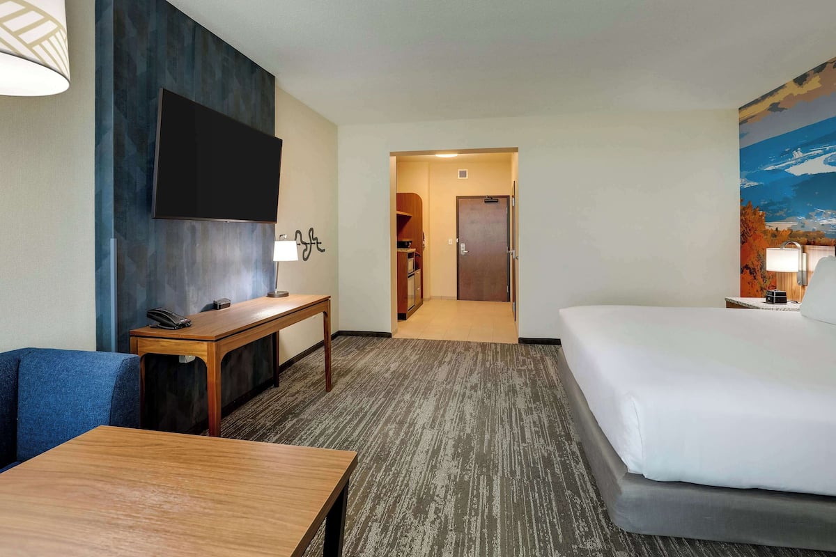 Ein Hotelzimmer mit einem großen Bett, einem Schreibtisch mit Telefon, einem flachbildfernseher an der Wand und einem Bild an der Wand.