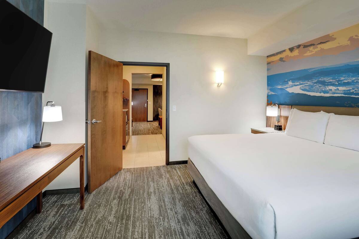 Ein Hotelzimmer mit Bett, Schreibtisch, Fernseher und einem Bild an der Wand.