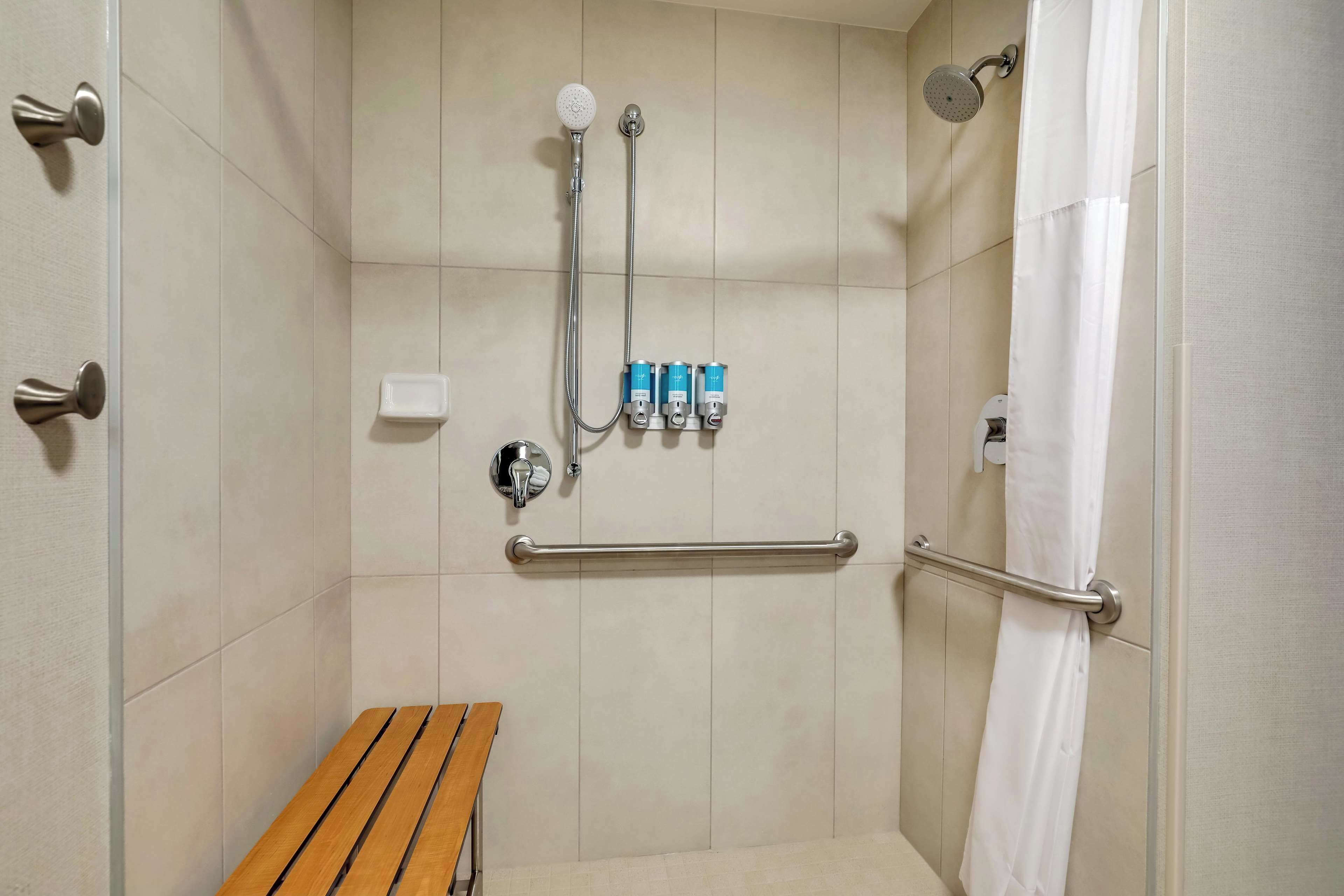 Un espace douche équipé d’un banc, de barres d’appui et d’un pommeau de douche à main.