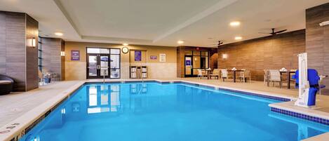 An indoor swimming pool with a 40 ft depth, surrounded by lounge chairs and tables, and a reception area with a clock and informational signs.
